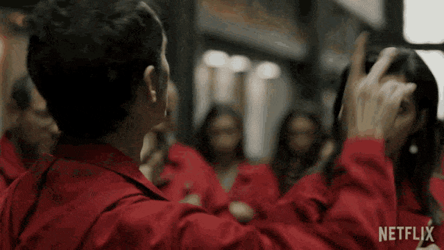La casa de papel, hombre con capa roja llevándose el dedo a la boca como diciendo «shhhh».