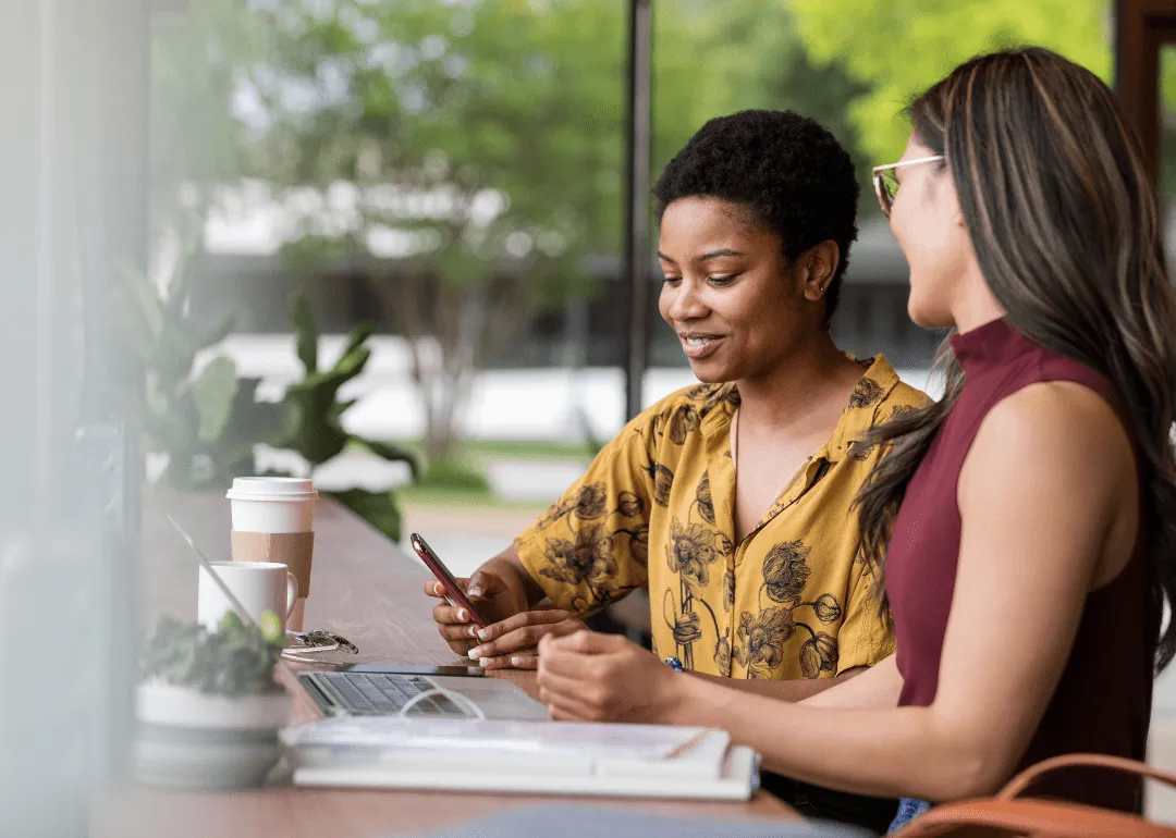 Zwei Frauen arbeiten gemeinsam an ihrem Laptop und Smartphone.