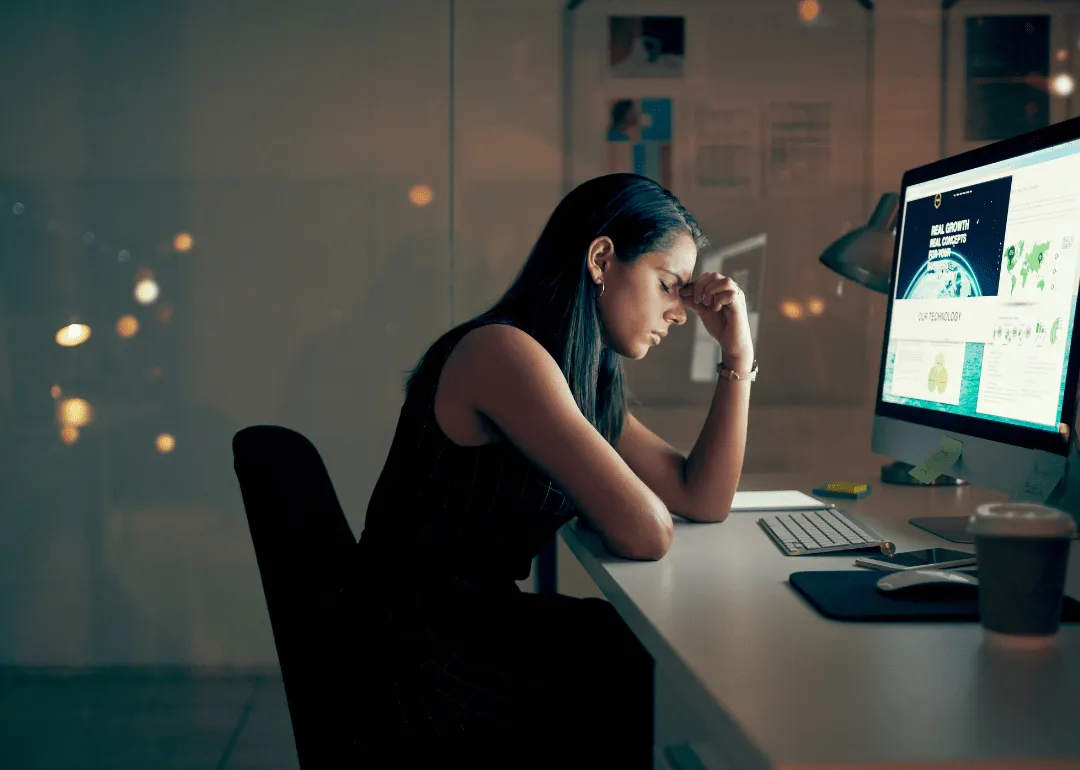 Eine Frau, die müde und gestresst an der Front eines Computers sitzt
